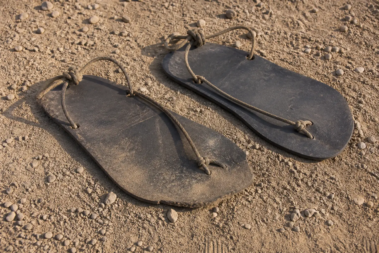 A pair of worn running sandals, flat rubber soles tied on with cord