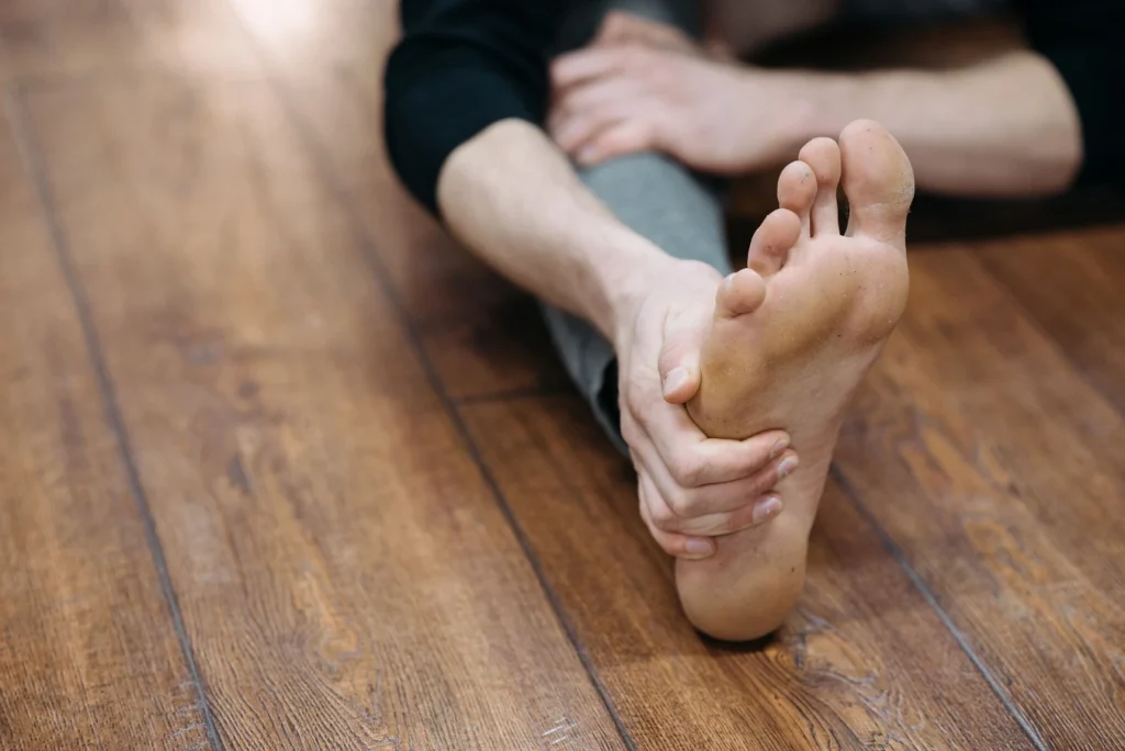 Person stretching their bare foot on a wooden floor, illustrating plantar fasciitis pain relief