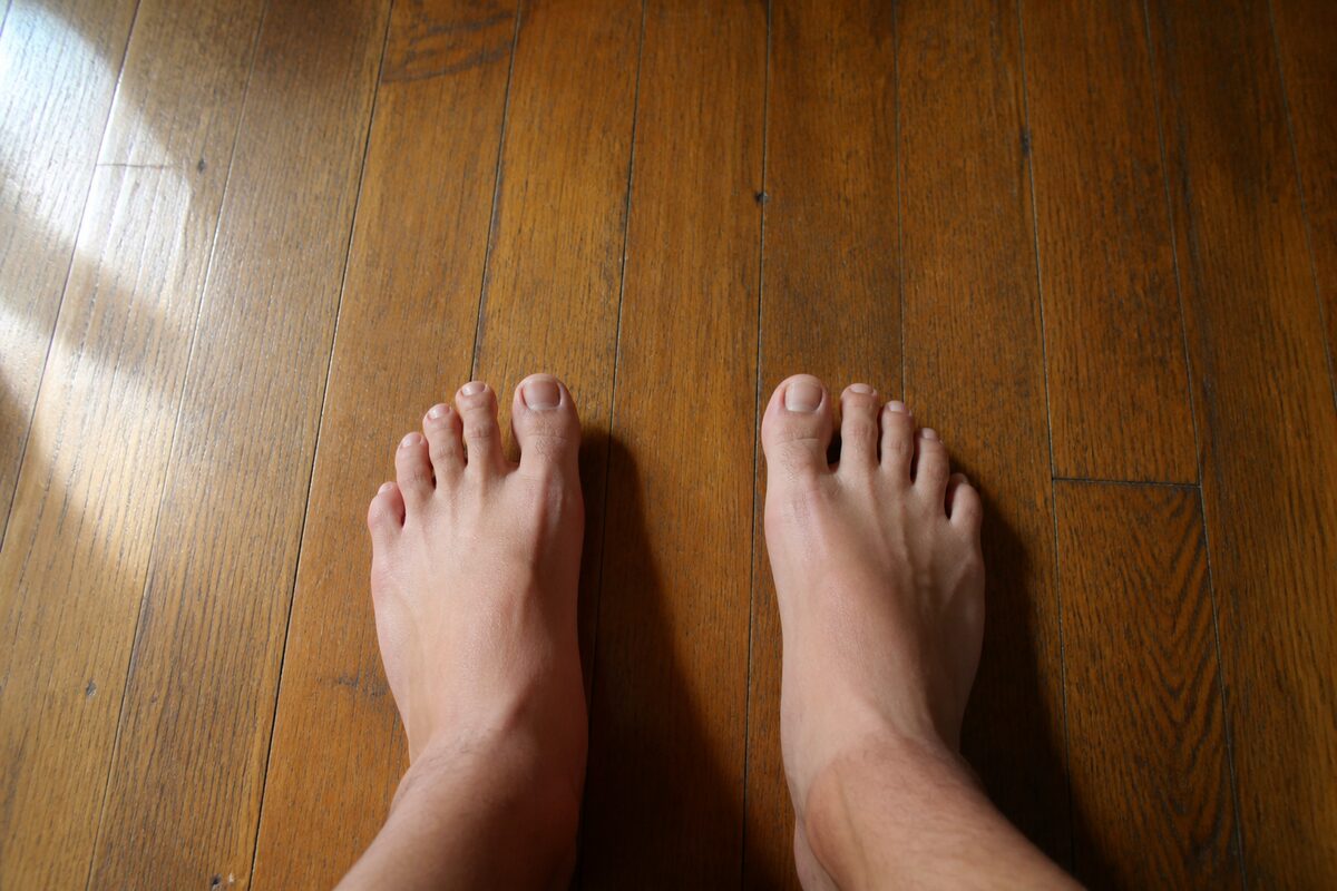 Bare feet standing on a wooden floorboard, toes relaxed and spread