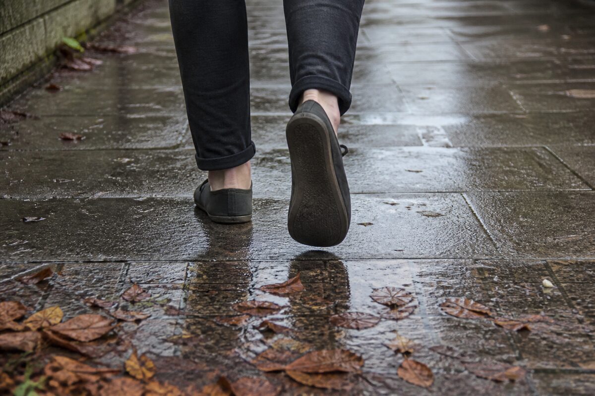 Low angle view of someone walking away on a wet pavement in thin soled barefoot shoes