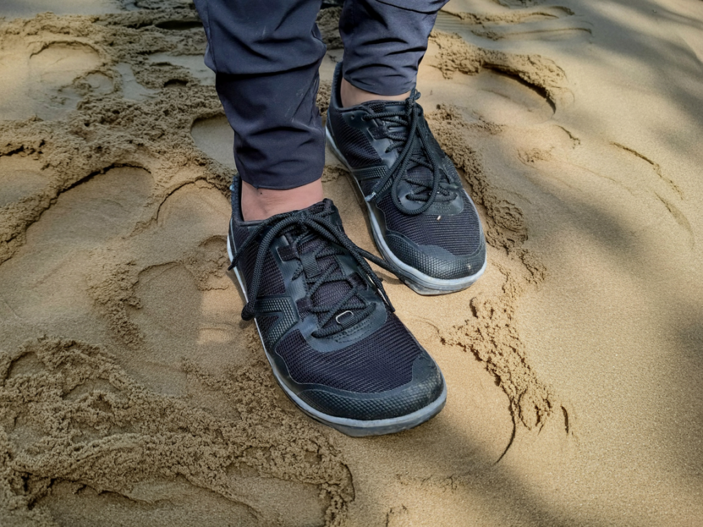 Close-up of the black Xero Shoes Scrambler Low EV being worn on a sandy beach, highlighting its front and laces.