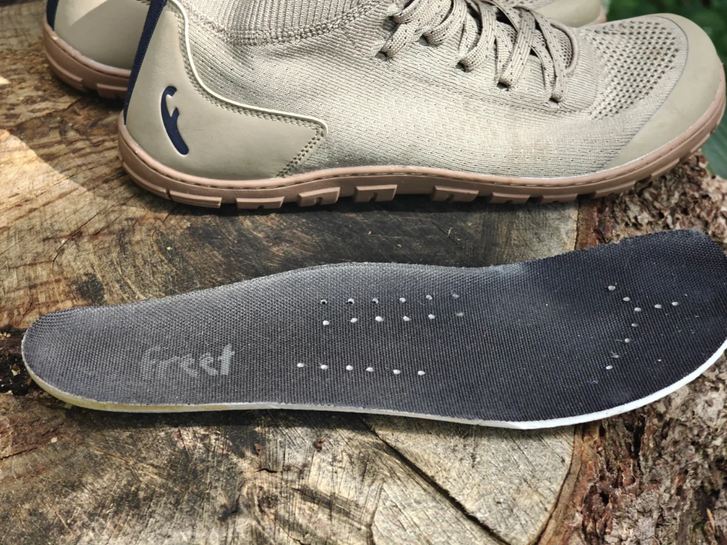Removable insole laid flat on a tree stump in front of the Freet Danum shoe, showing ventilation holes and heel lettering.
